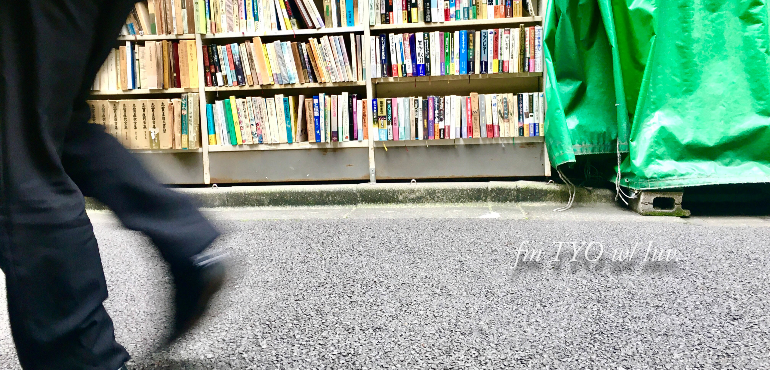 路面に設置された古本屋の書棚の前を歩く男性の足